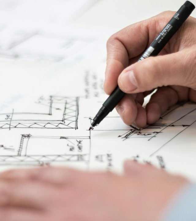 Close-up of hand drawing intricate technical designs on blueprint with pen, ideal for engineering or architecture themes.